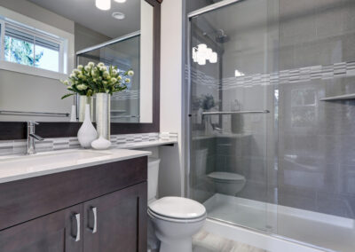Sleek, modern bathroom with toilet, sink, cabinet, and walk-in shower with a glass door.